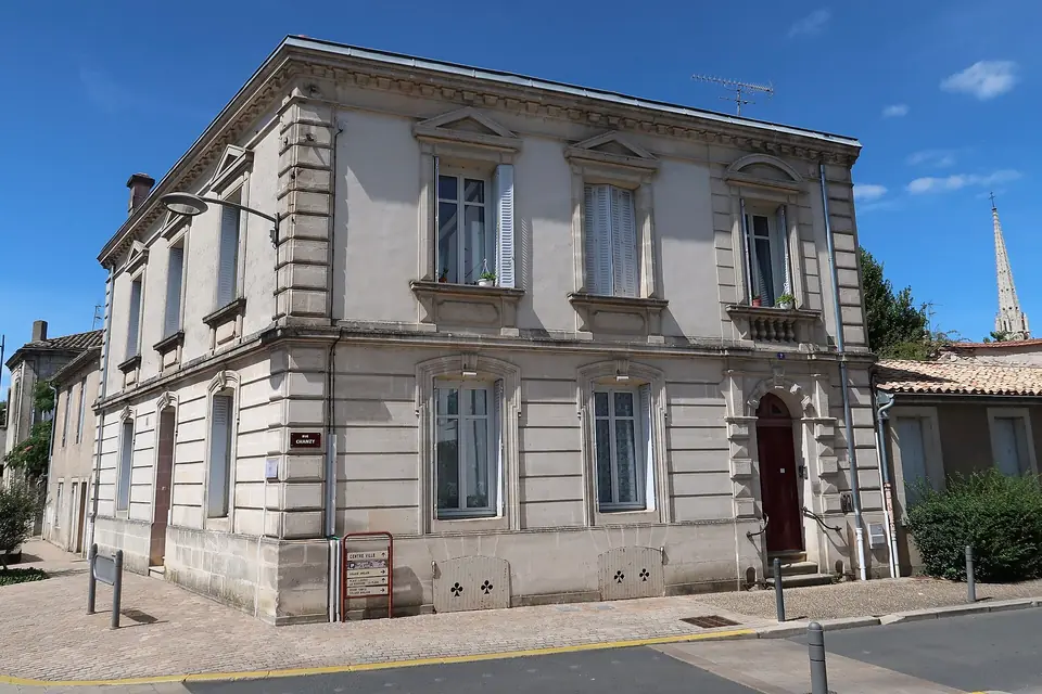 Maison en pierre claire au 2 rue Chanzy à Sainte-Foy-la-Grande, avec la flèche de l'église Notre-Dame en arrière-plan.